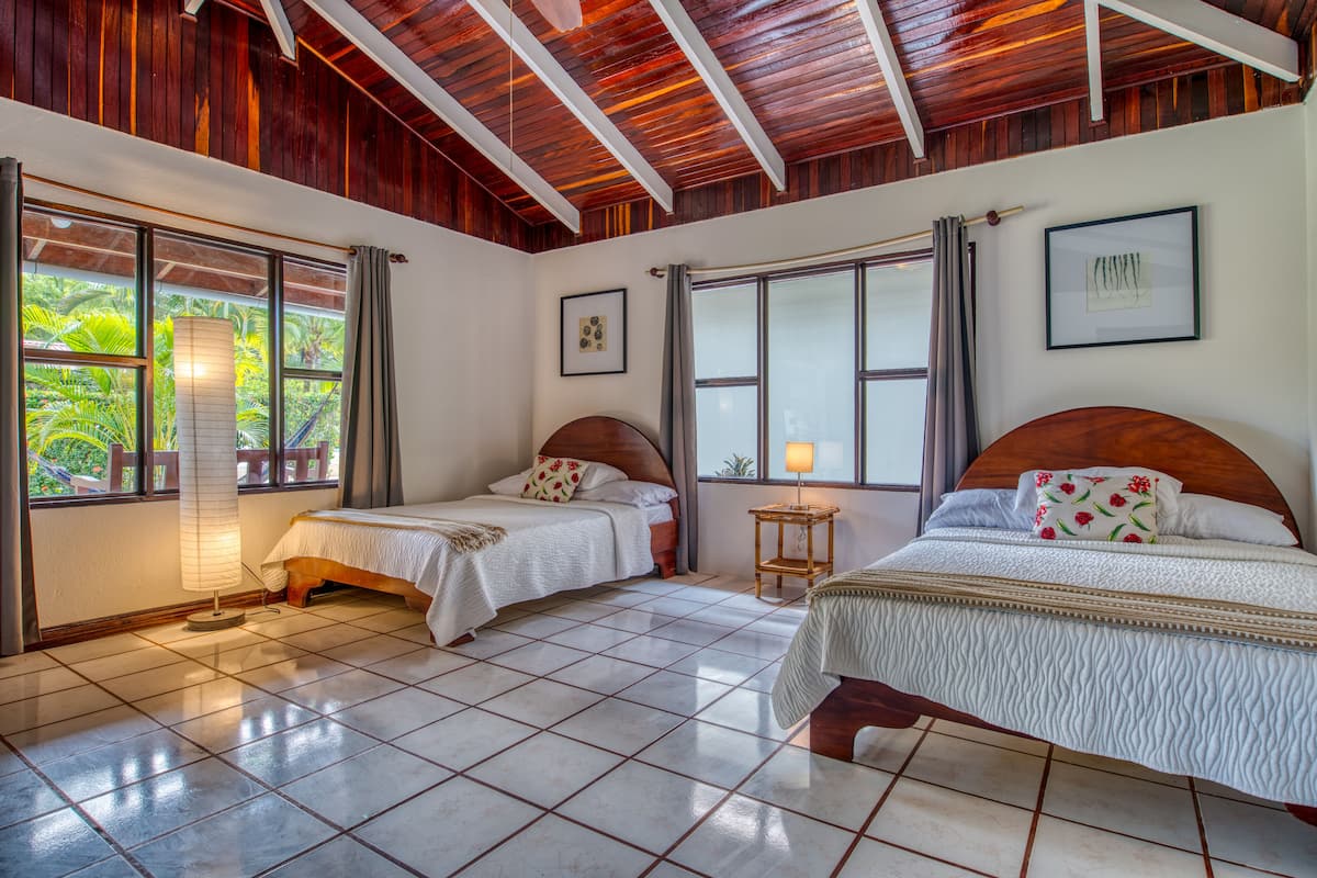 A room with two beds, large windows, and a wooden ceiling.