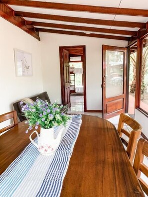 A wooden dining table with a vase of flowers, a striped runner, and a bench with cushions.
