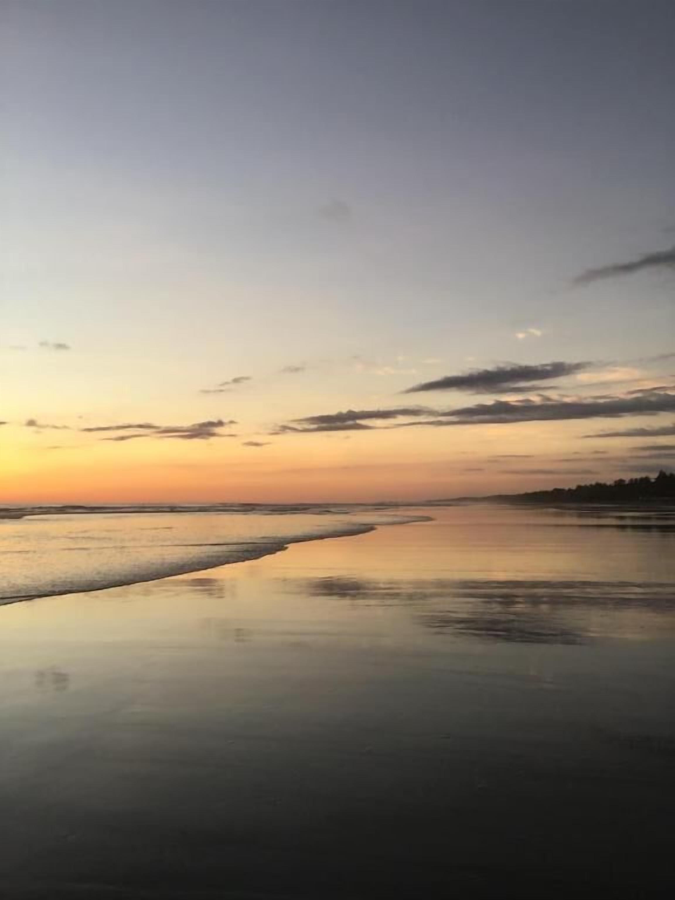 En strand ved solnedgang med roligt vand, der spejler himlen.