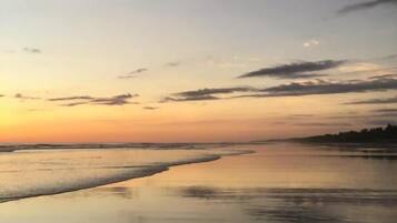En strand ved solnedgang med roligt vand, der spejler himlen.