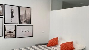 A modern bedroom with a gray sofa bed, a striped bedspread, and two orange pillows. There are framed pictures on the wall, including a typewriter and a cityscape. - Lago Azzurro modern aparment with lake view and ba (Verbania)