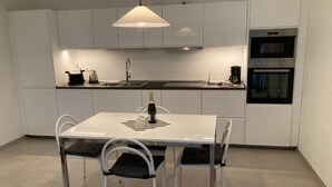 A modern kitchen with white cabinetry, a stainless steel oven, and a dining table with four chairs. - Lago Azzurro modern aparment with lake view and ba (Verbania)