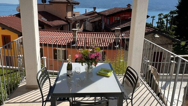 A balcony with a table set for two, overlooking a coastal town with terracotta roofs and a view of the sea. - Lago Azzurro modern aparment with lake view and ba (Verbania)