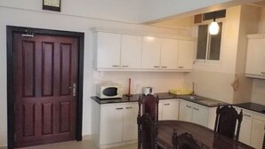 A compact kitchen with white cabinets, a microwave, and a dining table with chairs. - Newly Renovated Spacious 2 Bedroom Apartment (Colombo)