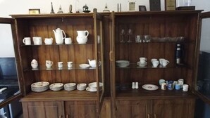 A wooden cabinet with shelves holding various white ceramic items like teapots, cups, and plates. - Newly Renovated Spacious 2 Bedroom Apartment (Colombo)