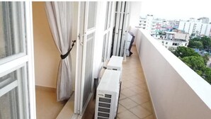 A balcony with a view of a cityscape, a window with a curtain, and an air conditioning unit. - Newly Renovated Spacious 2 Bedroom Apartment (Colombo)