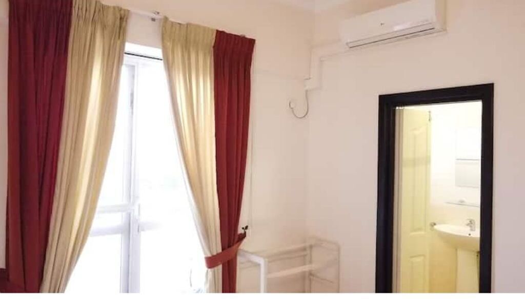 A room with a window, a white radiator, and a door leading to a bathroom with a sink.