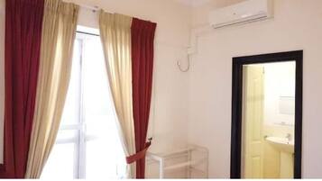 A room with a window, a white radiator, and a door leading to a bathroom with a sink.