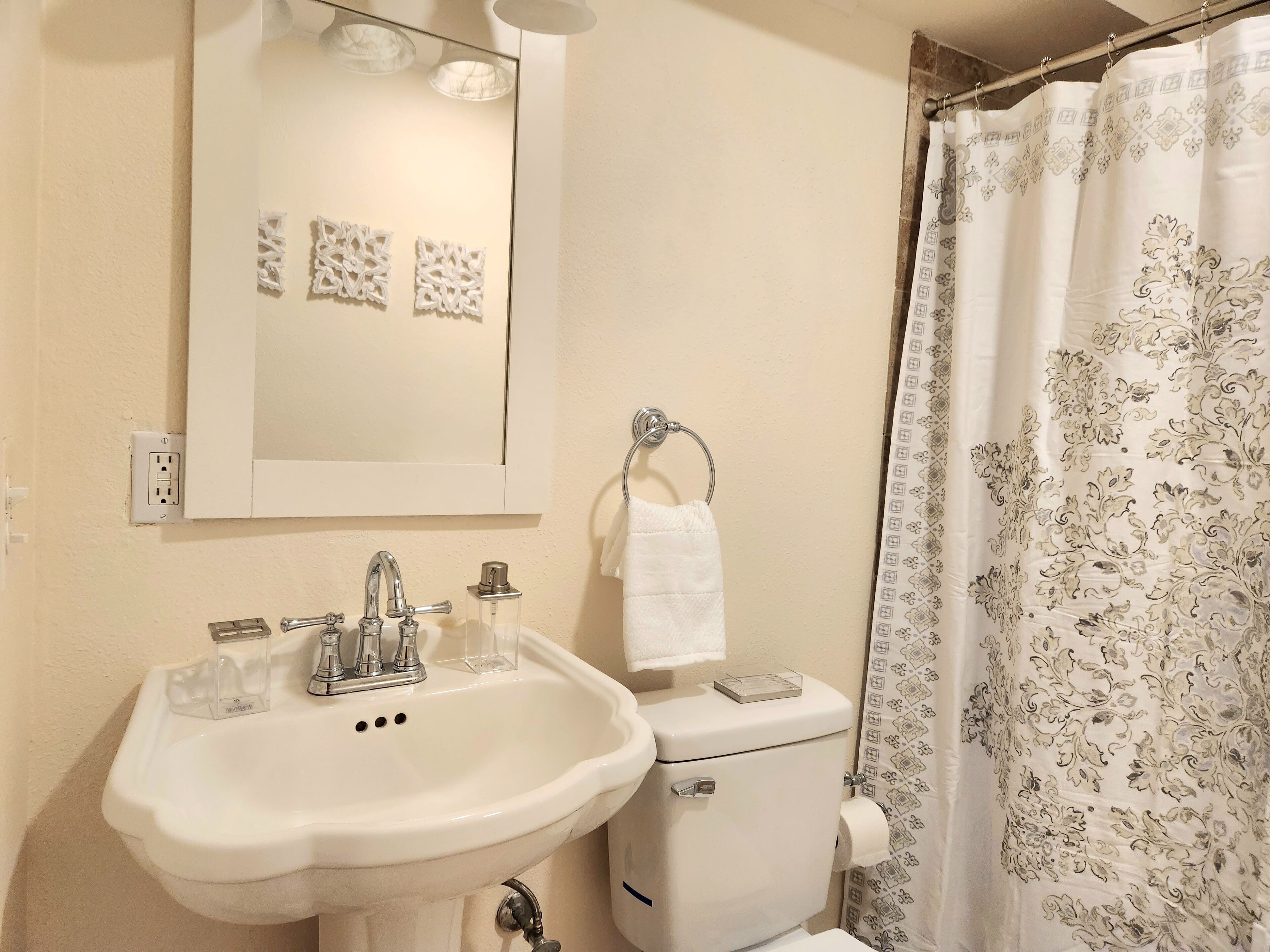 Une salle de bain avec un lavabo blanc, un miroir, des toilettes et un rideau de douche à motifs floraux.