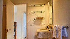 Een badkamer met een wastafel, spiegel, handdoekhouder en glazen planken.