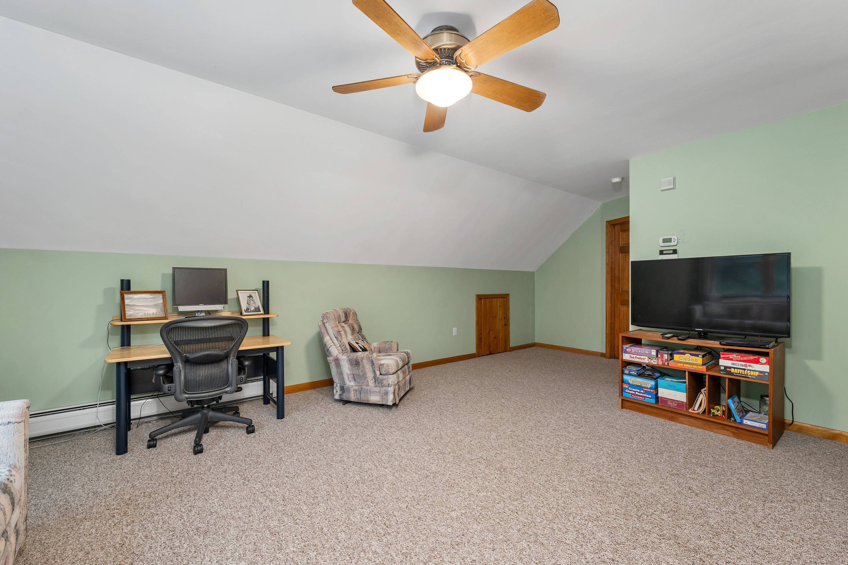 A room with a ceiling fan, a desk with a computer, a chair, a television, and a bookshelf.
