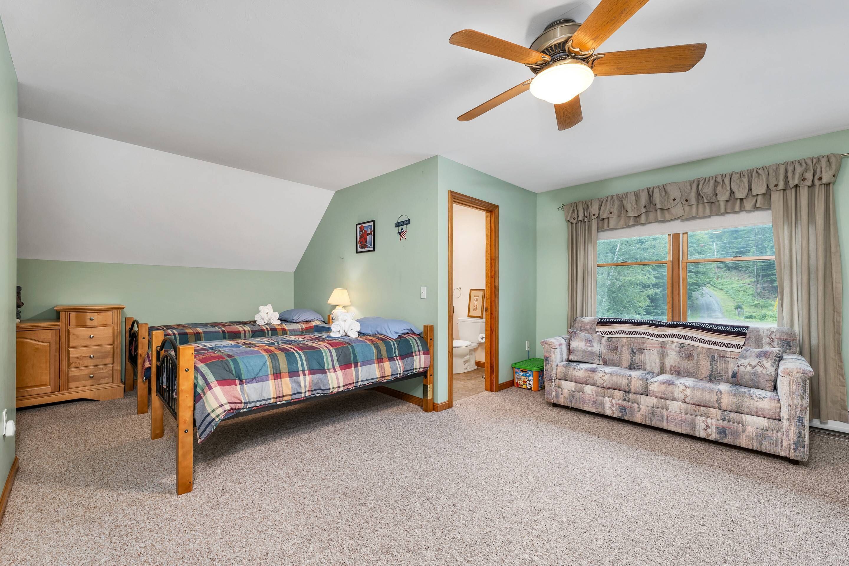 Une chambre avec deux lits, une commode en bois, un ventilateur de plafond et une fenêtre avec des rideaux.