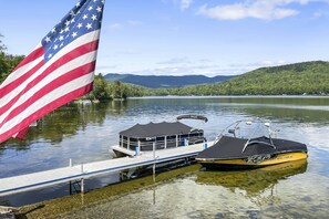 A dock with two boats, an American flag, and a lake with hills in the background.