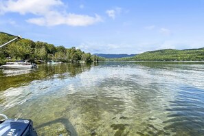 A boat on a calm lake with clear water, surrounded by trees and hills.