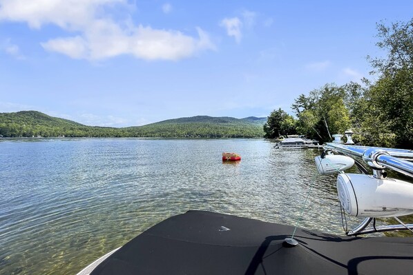 A boat docked at a marina with clear water, a red buoy, and hills in the background.