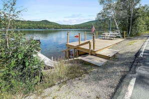 A wooden dock extending into a calm lake, with a picnic table and an American flag on the right.