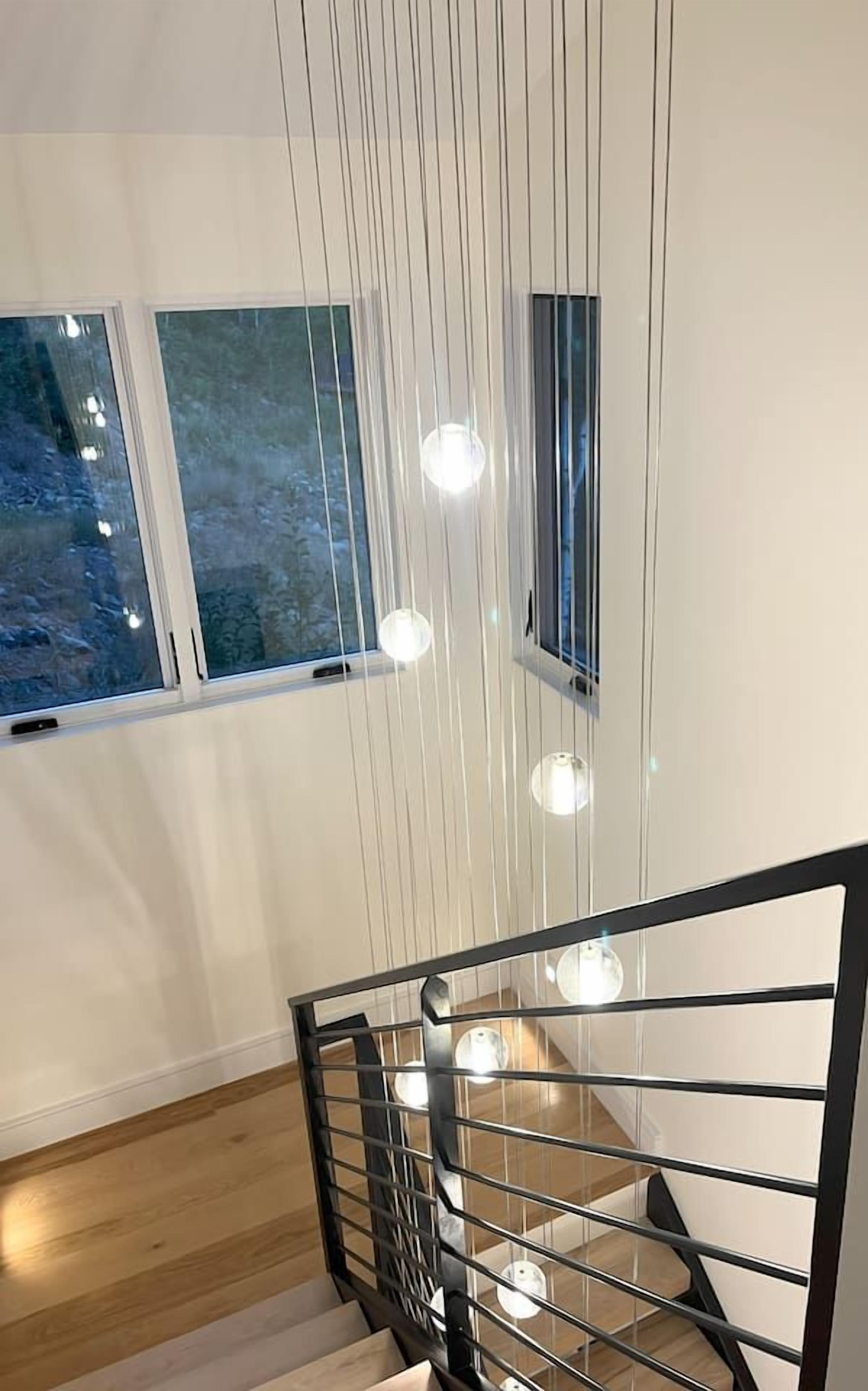 A modern staircase with a metal railing, wooden steps, and pendant lighting.