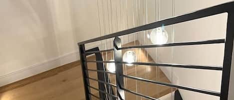 A modern staircase with a metal railing, wooden steps, and pendant lighting.