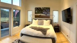 Une chambre à coucher avec un grand lit, un téléviseur fixé au mur et un tableau représentant un arbre.