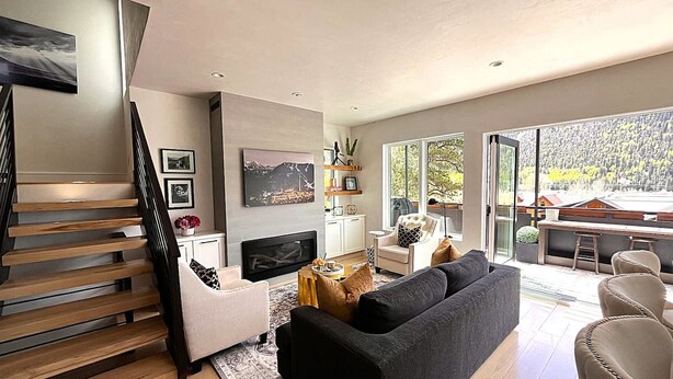Un salon moderne avec un escalier, une cheminée et une grande fenêtre donnant sur l’extérieur.