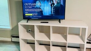 A television on a white entertainment unit in a room with a window and a wooden floor. - Studio Unit in Kouts/Valparaiso 3 (Kouts)