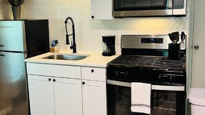 A compact kitchen with white cabinets, a stainless steel refrigerator, a microwave, a stove, and a sink. - Studio Unit in Kouts/Valparaiso 3 (Kouts)