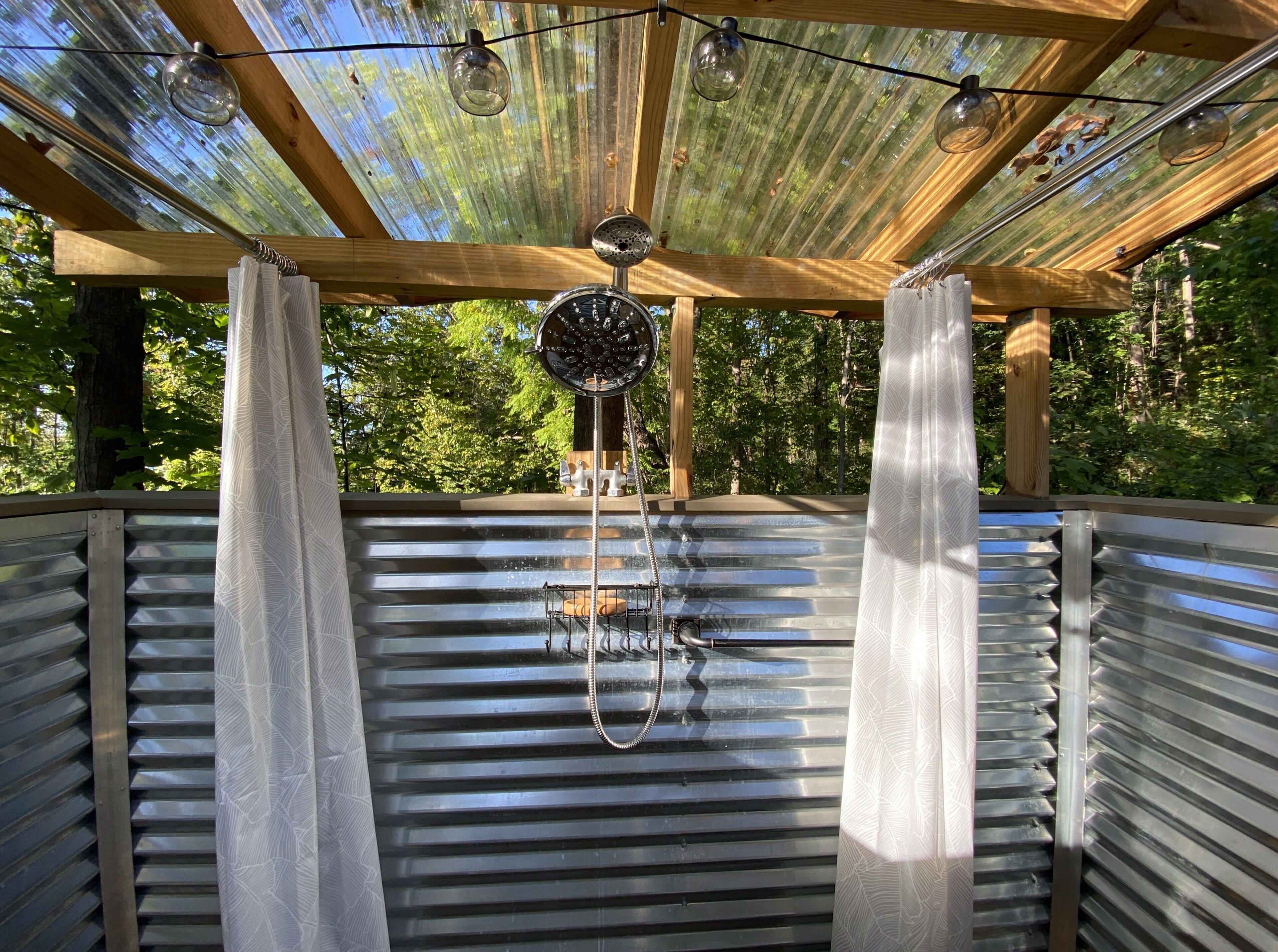 Un espacio al aire libre techado con techo metálico, vigas de madera y lámparas colgantes.