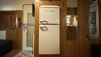 A compact room with a wooden door, a white Galanz refrigerator, a small bed, and a patterned rug.
