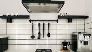 Eine moderne Küche mit Gasherd, Kaffeemaschine, hängenden Küchenutensilien und Dunstabzugshaube.