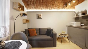 A modern living room with a grey sofa, a small round table with a plant, and a kitchen area with a microwave.