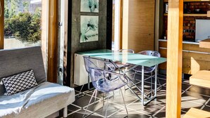 Un intérieur moderne avec une table à manger en verre, des chaises transparentes, un canapé agrémenté de coussins à motifs et un escalier avec des rampes en bois.