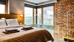 Hotelkamer met een groot bed, hoofdeinde, nachtkastje, lamp en uitzicht door een groot raam.