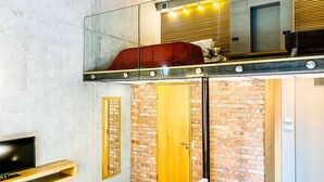 Ett modernt rum med en säng på ett loft, en tv på ett träställ och en vägg av tegelsten.