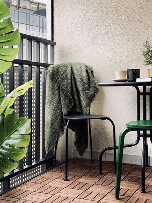Uma varanda com uma cadeira, uma mesa e um vaso de planta.