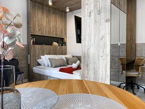 A modern bedroom with a wooden headboard, a bed with white bedding, a red throw blanket, and a small shelf with decorative items. - Rakowicka 6/38 (Kraków)