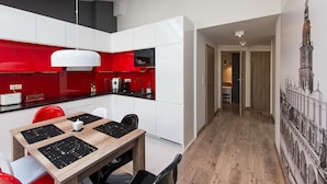 Una cocina moderna con armarios rojo y blanco, un comedor con mesa de madera y sillas negras, y un pasillo que lleva a un dormitorio.