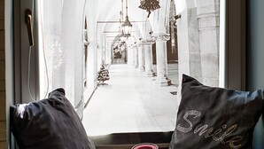 Vista a través de una ventana con dos almohadas en un banco, una vela y un suelo estampado.