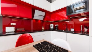 Una cocina moderna con armarios rojos, encimera negra y mesa de comedor blanca.