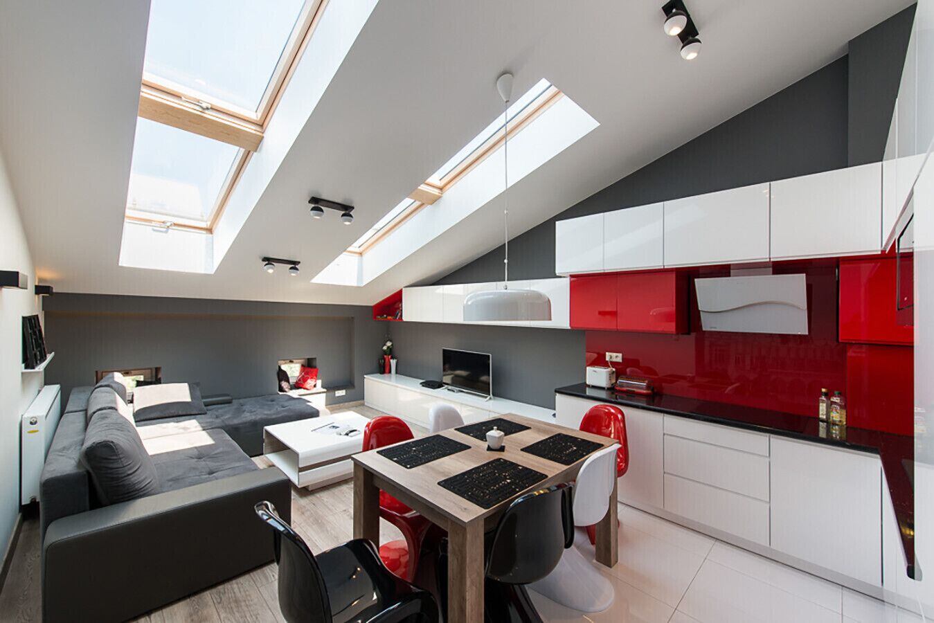 A modern apartment with a dining area, kitchen, and living space, featuring skylights and a combination of white and red cabinetry.