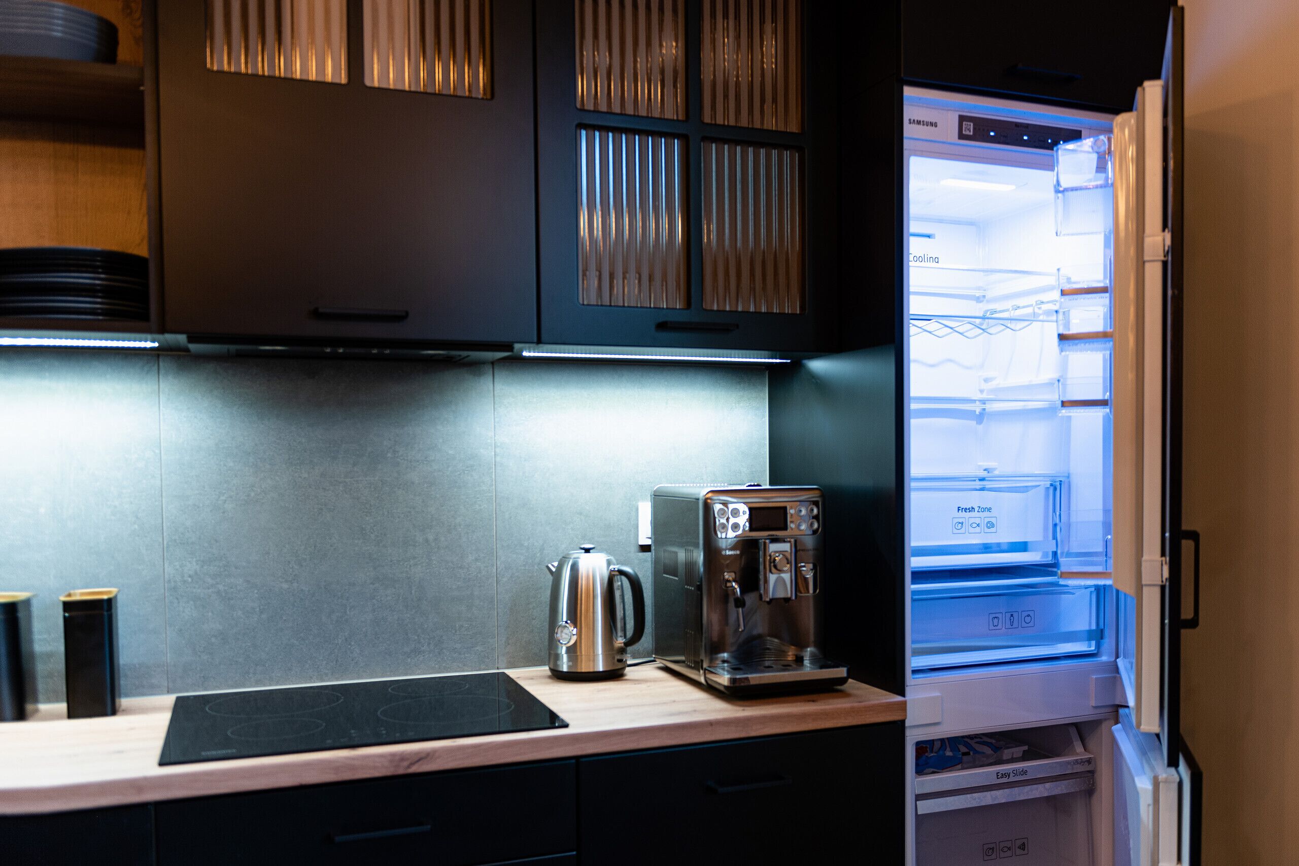 A kitchen with a built-in refrigerator, a coffee maker, and a kettle on the counter.