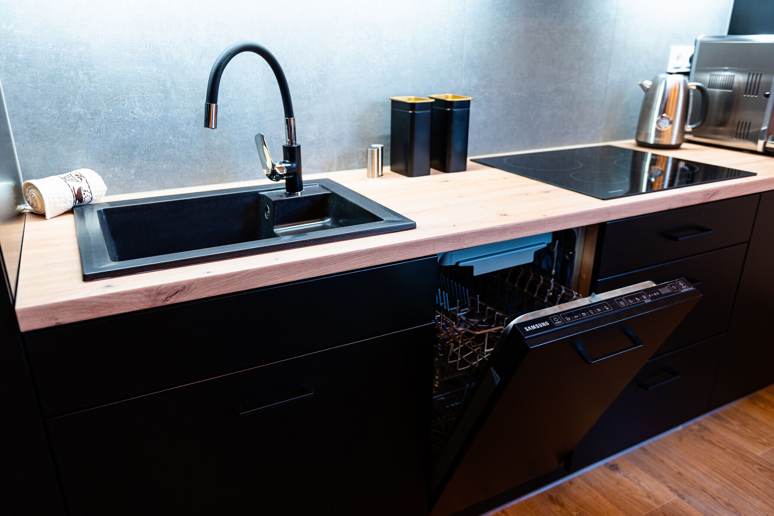 Una cucina con lavello nero, piano di lavoro in legno e lavastoviglie.