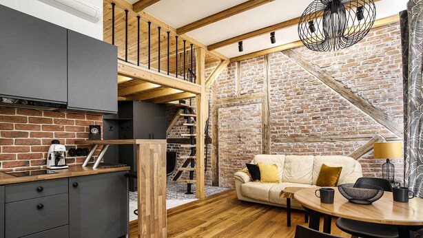 Um espaço de estar estilo loft com cozinha, área de jantar e escada que dá acesso a um mezanino.