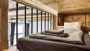 Quarto de cabana de madeira com uma cama, almofadas e vista através de uma grande janela.