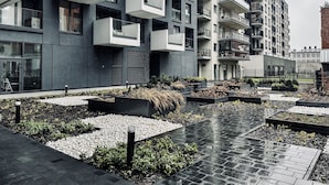 A modern apartment building with balconies, a courtyard with plants, and a paved walkway. - Zabłocie 27/34 (Kraków)