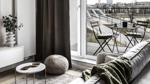 A modern living room with a large window, a sofa, a round table, and a plant. - Zabłocie 27/34 (Kraków)