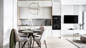 A modern kitchen with white cabinetry, a round dining table with chairs, and a TV mounted above the counter. - Zabłocie 27/34 (Kraków)