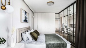 A modern bedroom with a bed, bedside table, and a view into the kitchen area. - Zabłocie 27/34 (Kraków)