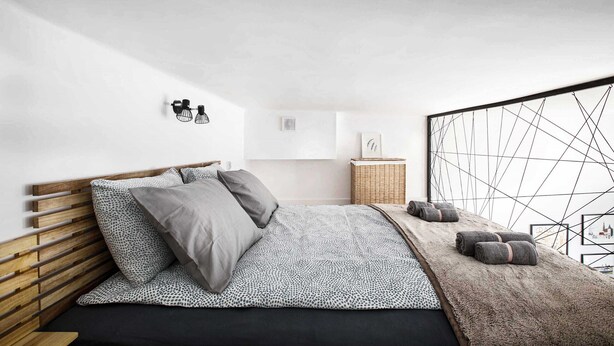 A modern bedroom with a wooden headboard, a patterned bedspread, and a view of the city through a geometric window design.