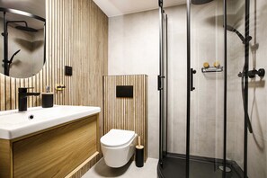 A modern bathroom with a wooden vanity, a toilet, a glass shower enclosure, and a black sink. - Apartament for 4 guests, Old Town, Train Station 2, Radziwiłłowska (Kraków)
