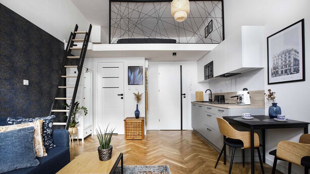 Un loft modern amb un llit d'entreplanta, una zona de menjador amb taula negra i una cuina amb armaris blancs.